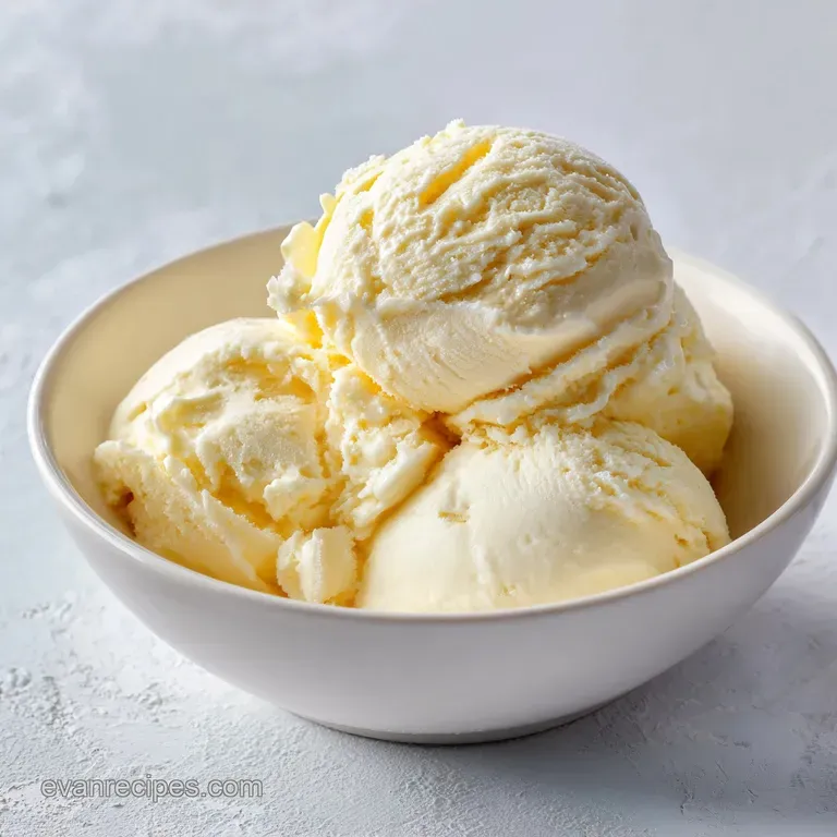 A scoop of smooth vanilla ice cream nestled in a chilled glass bowl, topped with a scattering of fresh mint.